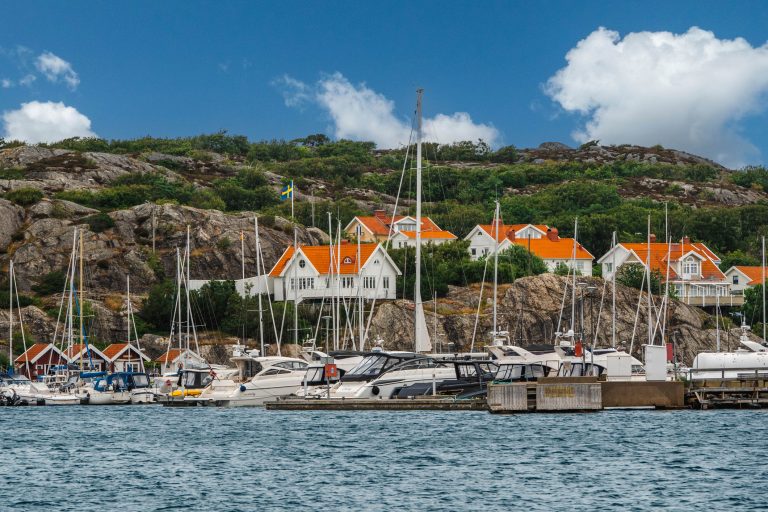 the-coastal-town-of-marstrand-in-southwest-sweden-houses-with-orange-roofs-sit-on-a-rocky-slope-a-large-number-of-sailboats-are-moored-in-the-foreground